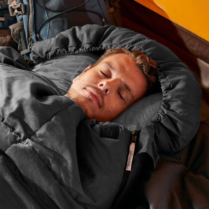 A man sleeping in a black Silentnight Adult Sleeping Bag whilst camping