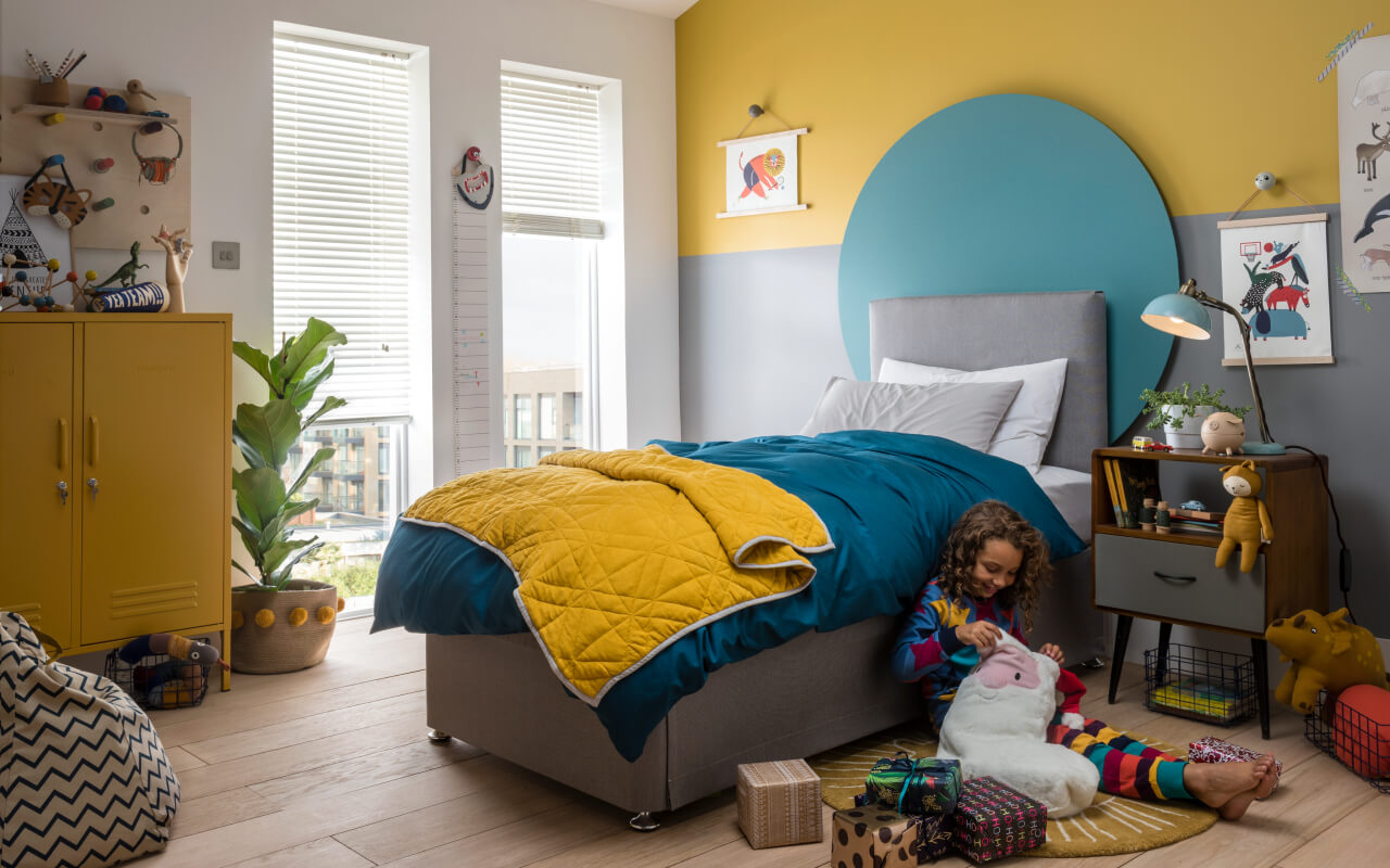 A child sat beside their bed opening Christmas presents